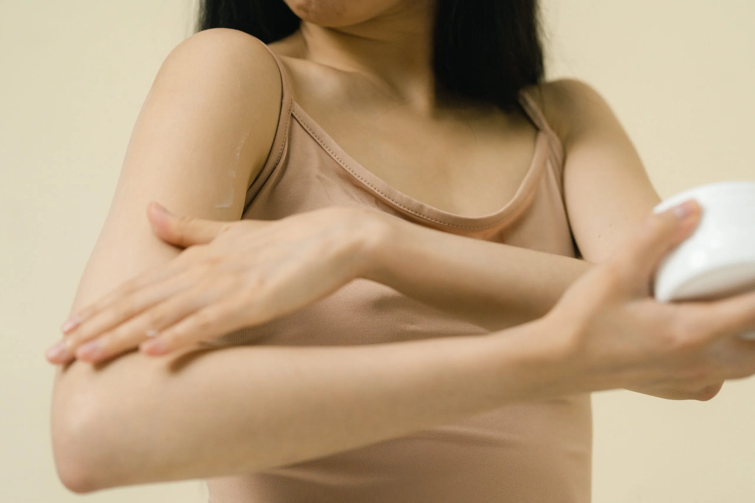 Close-up of a woman applying moisturizer to her arm in a studio setting.