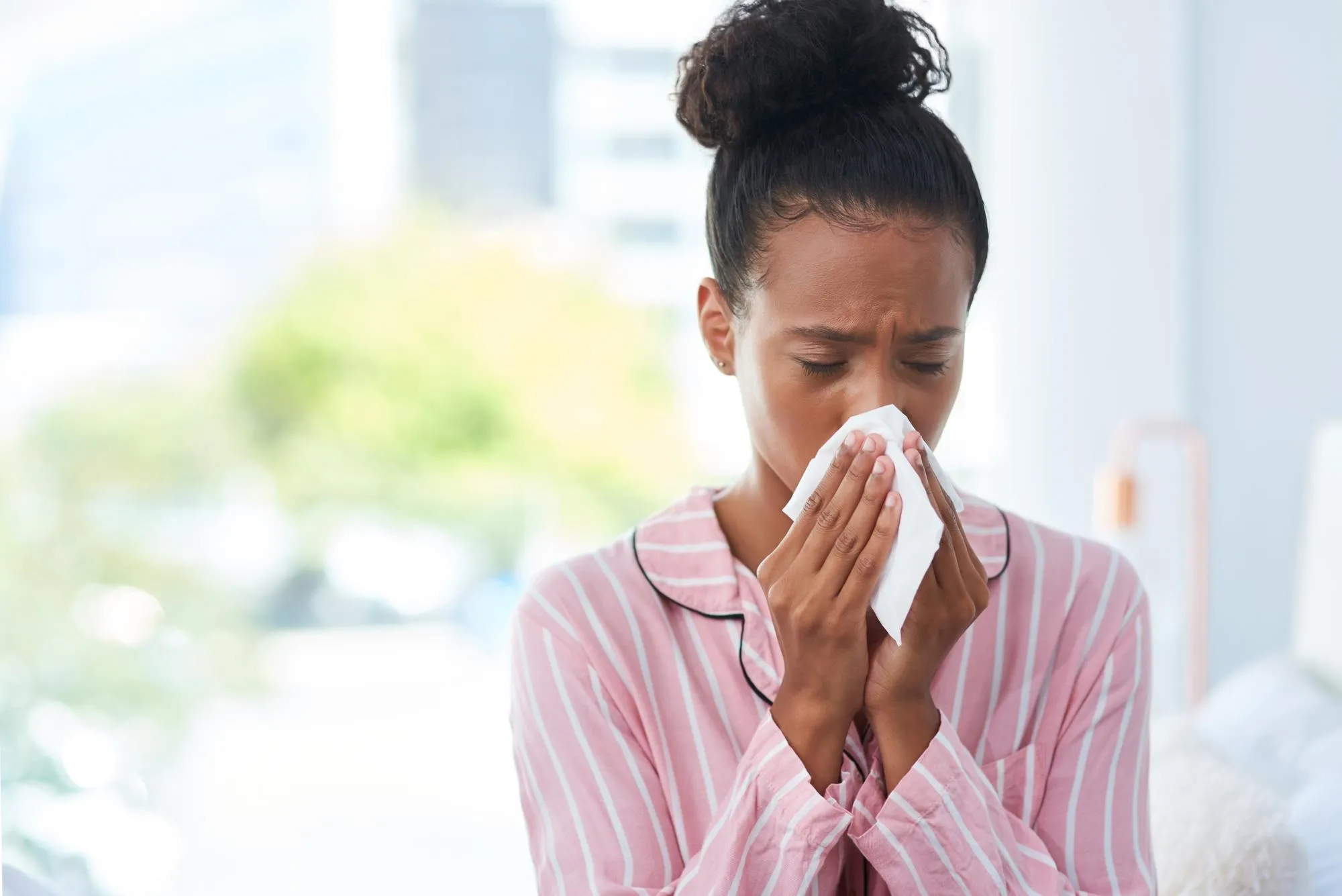 Sick black woman tissue and blowing nose in home for allergy season flu virus and sinus problem African girl toilet paper and sneezing with congestion for healthcare bacteria and pain in bedroom