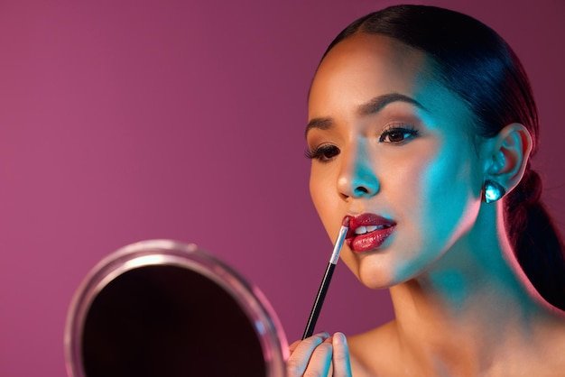 Woman makeup artist and lipstick in mirror with neon lights in studio for beauty and art deco Female person cosmetics and pride for futuristic design and creative by pink backdrop with glow