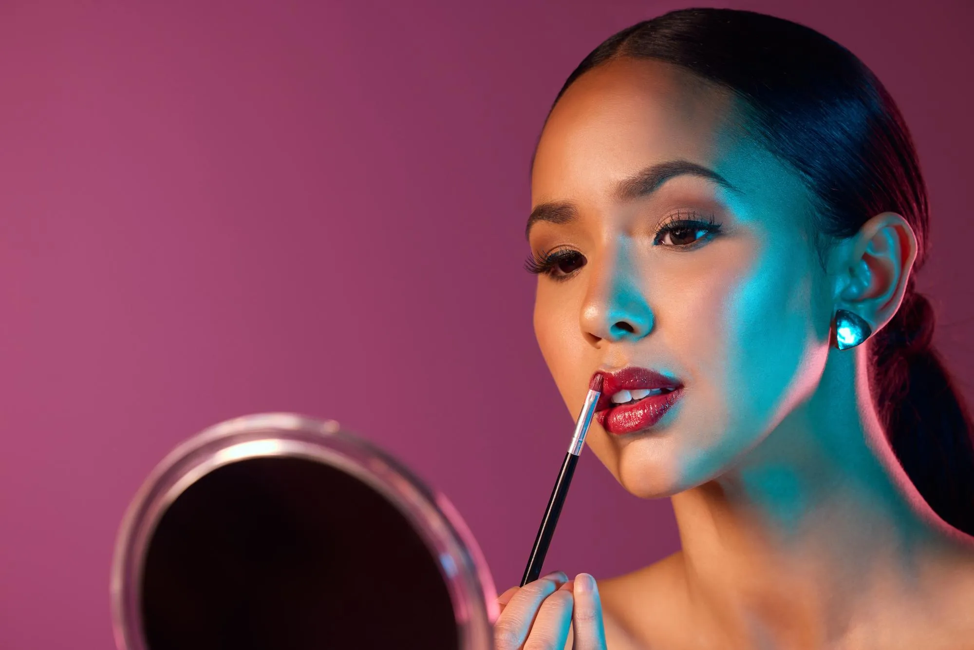 Woman makeup artist and lipstick in mirror with neon lights in studio for beauty and art deco Female person cosmetics and pride for futuristic design and creative by pink backdrop with glow