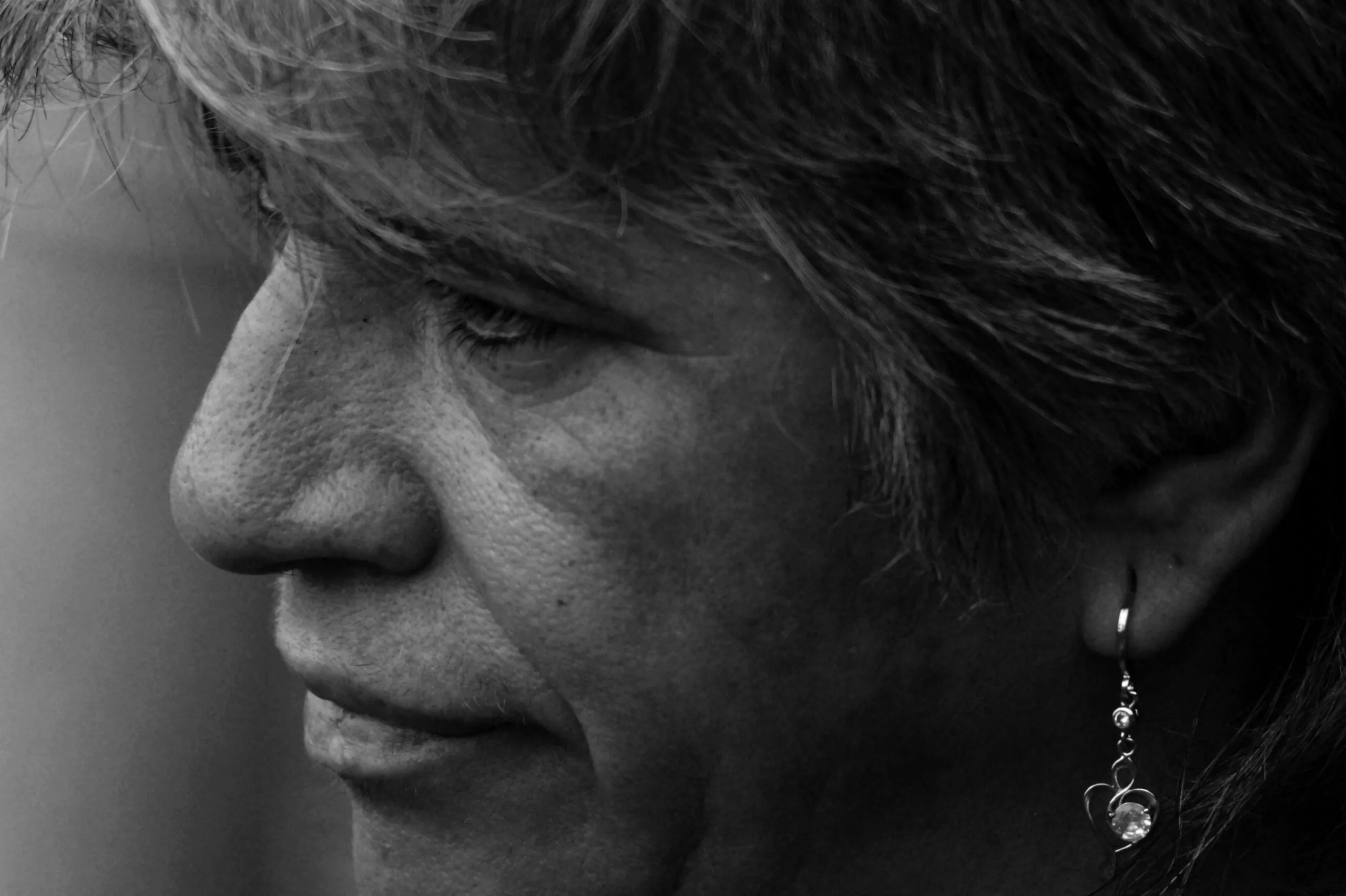 Artistic side profile portrait of an adult wearing a dangling earring in monochrome.