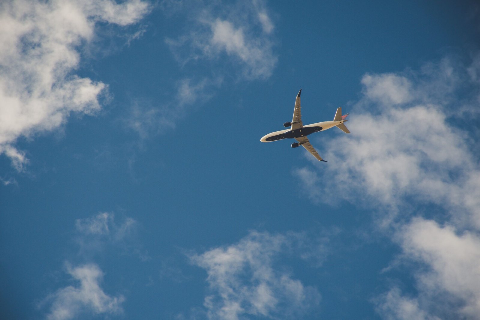 A commercial airplane flying high in the clear blue sky with clouds.