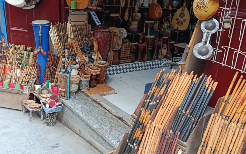 ​A detailed view of traditional Moroccan musical instruments in a shop in the Medina of Fes. The image highlights Krakebs (metal castanets used in Gnawa rituals), various types of drums (Taarija), and hand-crafted flutes. These instruments are fundamental to the rhythmic and spiritual rituals of Morocco, serving as essential tools for cultural expression and traditional ceremonies.
