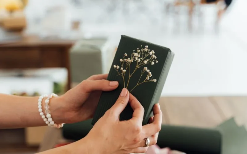 Close-up of hands holding a beautifully wrapped gift with floral accents, ideal for special occasions.