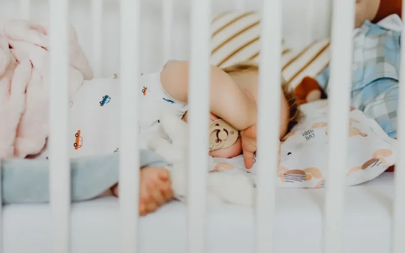 A baby peacefully sleeping with a pacifier in a cozy crib with plush blankets.