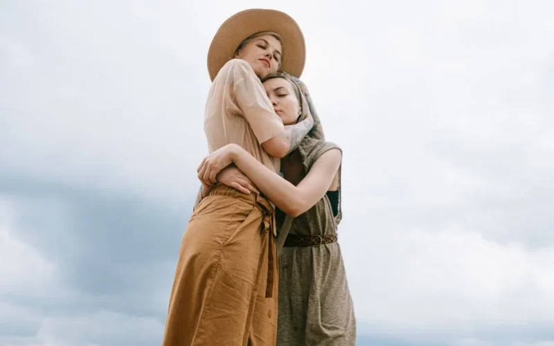 Two women share a comforting embrace outdoors, symbolizing love and togetherness.