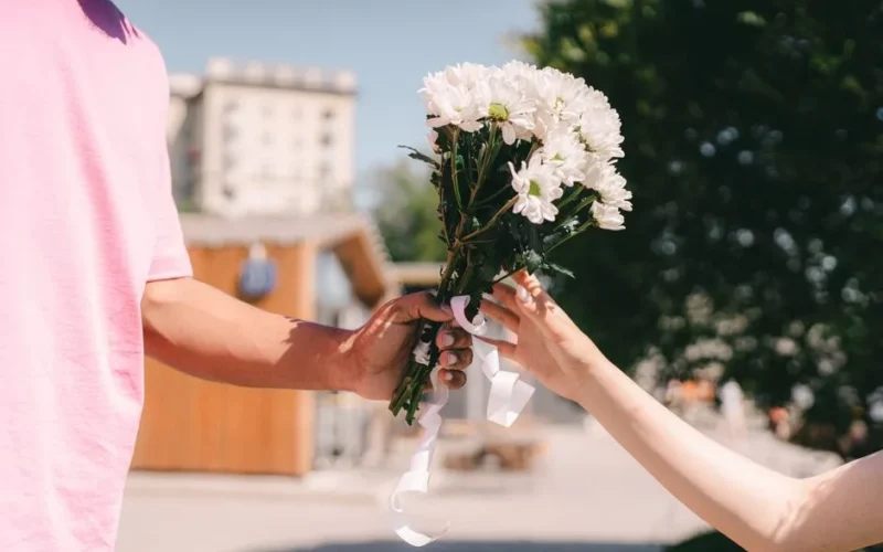 Close-up of couple exchanging a bouquet of white flowers on a sunny day.