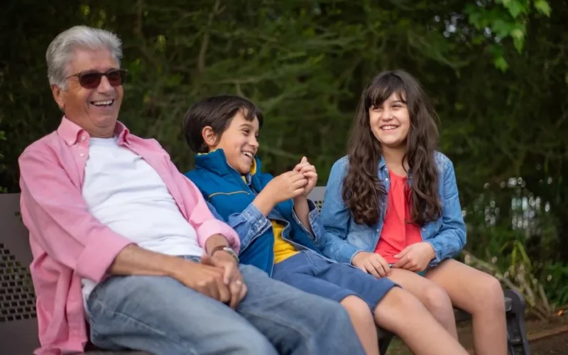 Grandfather with grandchildren laughing together on a park bench in Portugal.