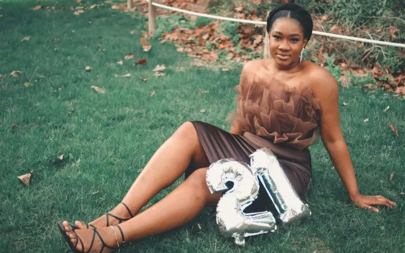 Stylish young woman celebrating her 21st birthday with silver balloons in a grassy outdoor setting.