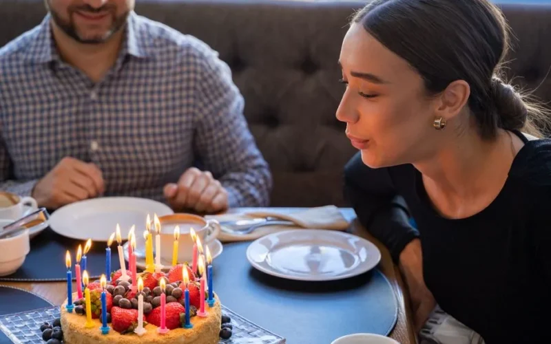 A woman joyfully blowing out candles on a fruit-topped birthday cake, sharing a festive moment.