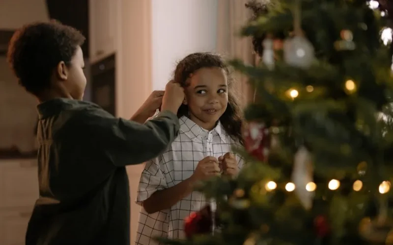 Two children cheerfully decorating a Christmas tree together at home, capturing the festive holiday atmosphere.