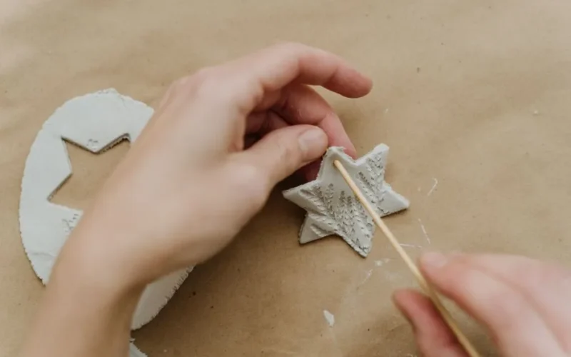 Hands crafting a star-shaped clay ornament using a stick on paper background.
