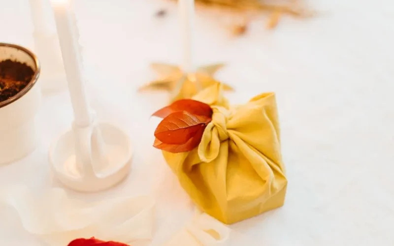 A beautifully wrapped gift with fall leaves, amidst cozy candles and natural decor.