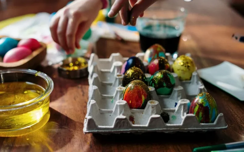 Hands decorating colorful Easter eggs with glitter and paint on a wooden table, capturing the festive spirit of the holiday.