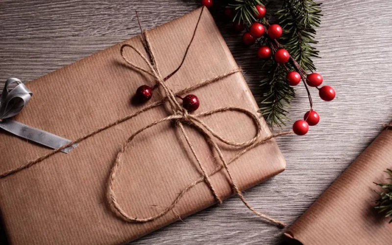 Beautifully wrapped Christmas present made of brown paper and twine, adorned with festive foliage and red berries.