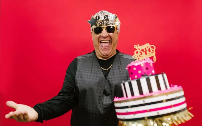 Joyful senior man celebrating birthday with cake against vibrant red background.