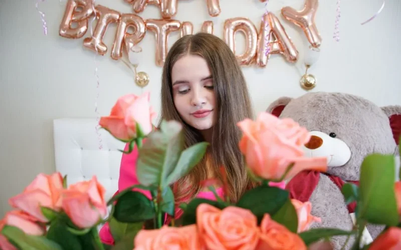A young woman celebrates her birthday surrounded by roses and festive balloon decorations.