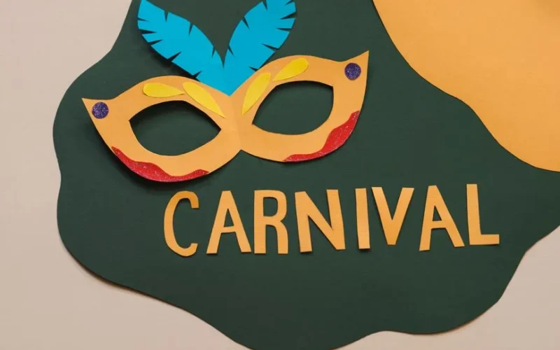 Vibrant paper cutout carnival mask with feathers and bold text on a colorful background.