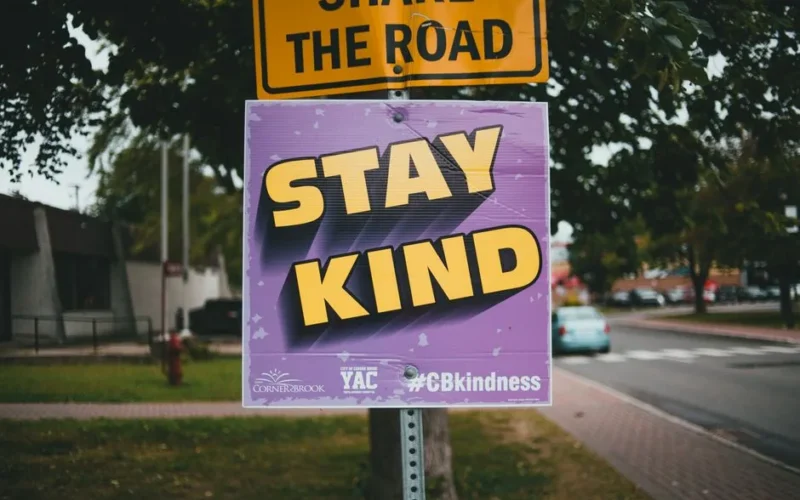 Close-up of a sign with 'Stay Kind' message on a city street.