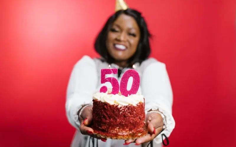 Joyful woman holding a cake with number 50 candles on a red background.