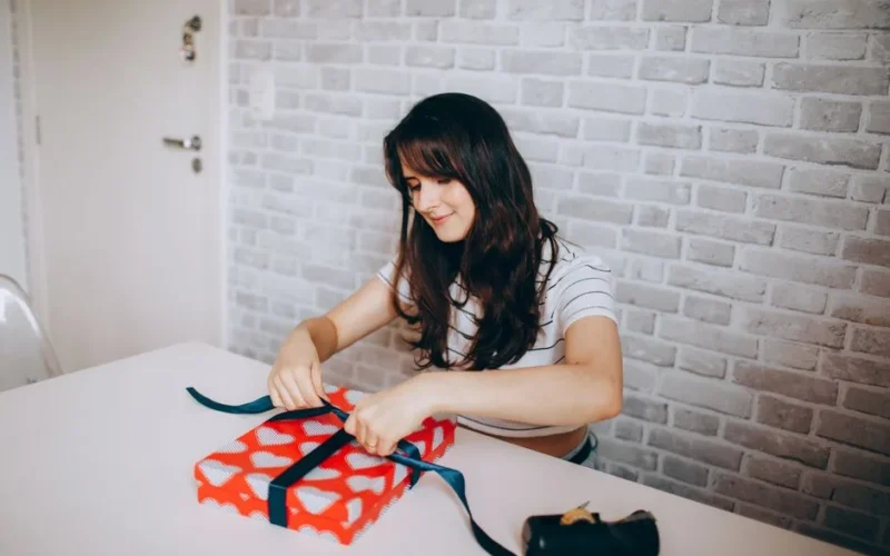 A young woman wrapping a heart-patterned gift indoors, expressing creativity and joy.