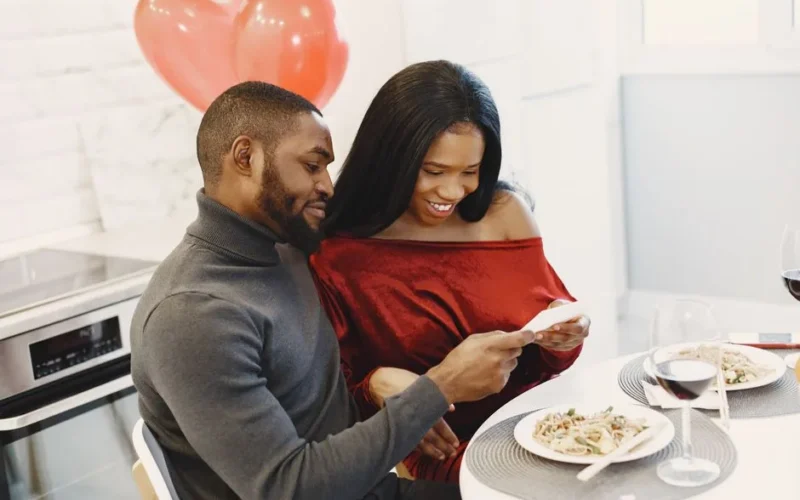 Couple enjoying a romantic dinner indoors with balloons and smiles.
