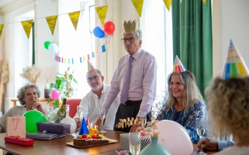 Smiling seniors celebrating a birthday party indoors with decorations and cake.