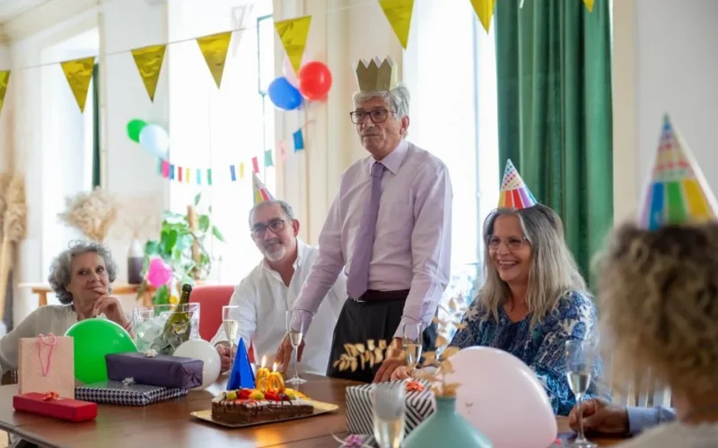Smiling seniors celebrating a birthday party indoors with decorations and cake.