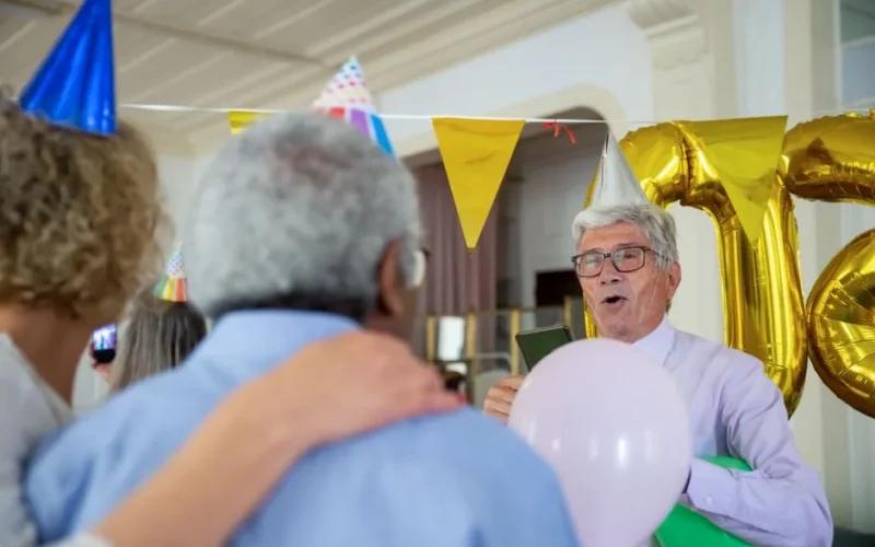 Elderly people celebrating a birthday indoors with party hats and balloons.
