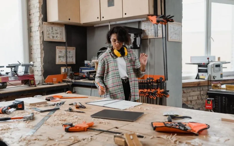A woman works in a woodworking workshop with tools and notes, crafting her latest project.
