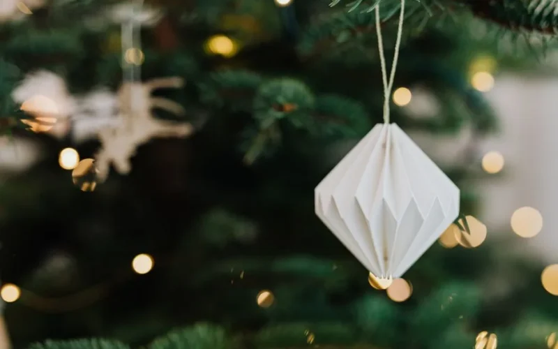 Elegant paper ornament hanging on a festive Christmas tree with blurred lights in the background.