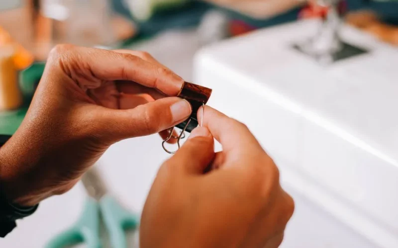 Detailed close-up of hands making leather crafts with sewing machine in the background.