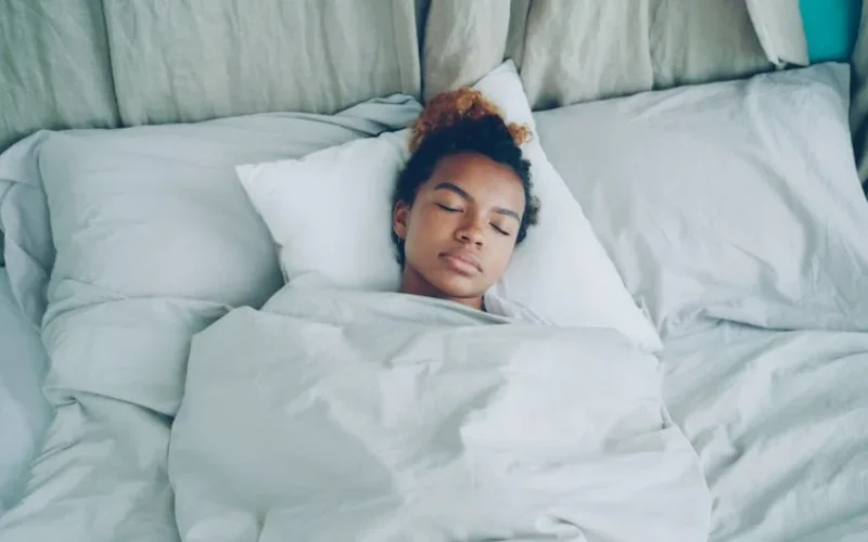 A serene woman peacefully sleeping in a cozy, white-sheeted bed.