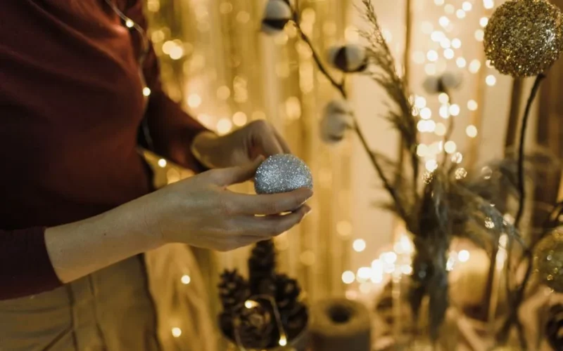 Close-up of a woman decorating with glittering baubles in a warm holiday setting.
