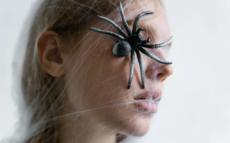 Close-up of a woman with a spider on her face wrapped in web. Concept of fear and phobia.