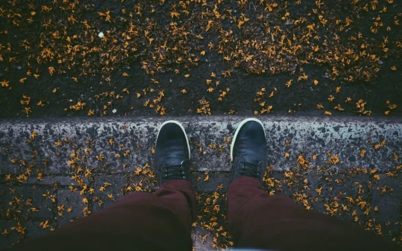 Top-down view of a person standing on a leaf-strewn pavement in autumn wearing stylish sneakers.