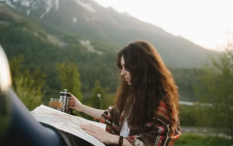 Brunette woman with map relaxing outdoors with coffee in a mountainous setting during sunset.