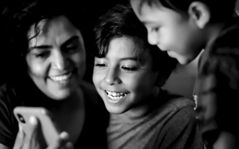 A joyful family moment with children and woman smiling at a phone screen, in black and white.