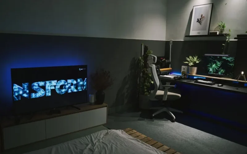 A sleek gaming room featuring a dark, contemporary setup with ambient blue lighting and multiple screens.