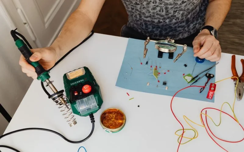 Close-up of a man skillfully soldering electronics with tools on a workbench.