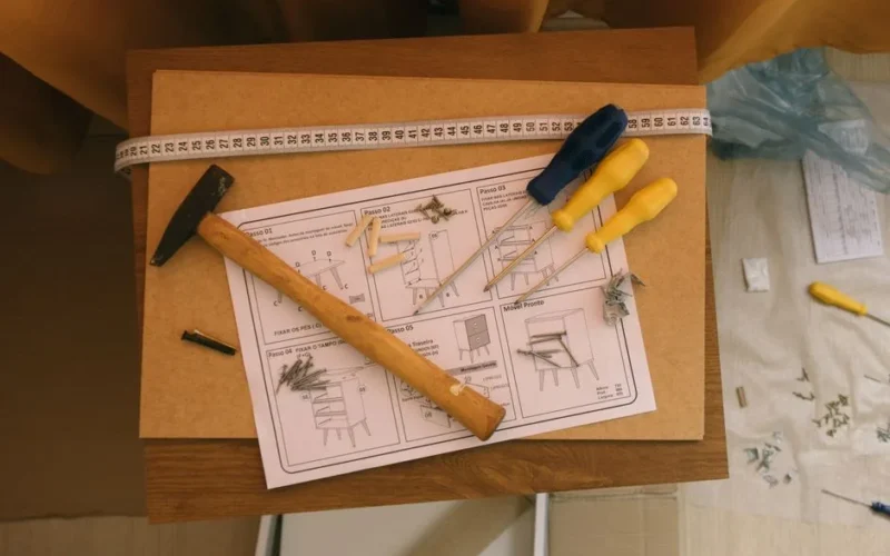 From above of paper instruction helping to assemble furniture with screwdrivers and hammer on top