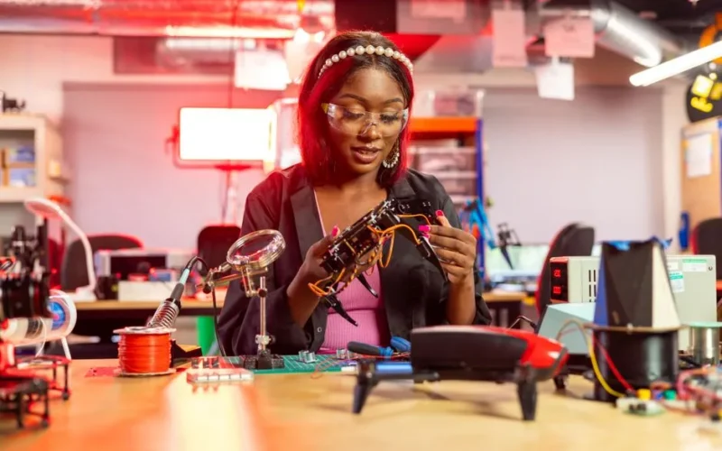 Black female engineer at desk assembling drones, showcasing electronics and technology in a modern lab setting.