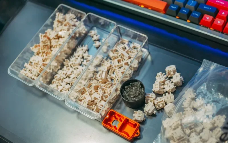 Close-up of mechanical keyboard switches and springs organized in containers on a desk setup.