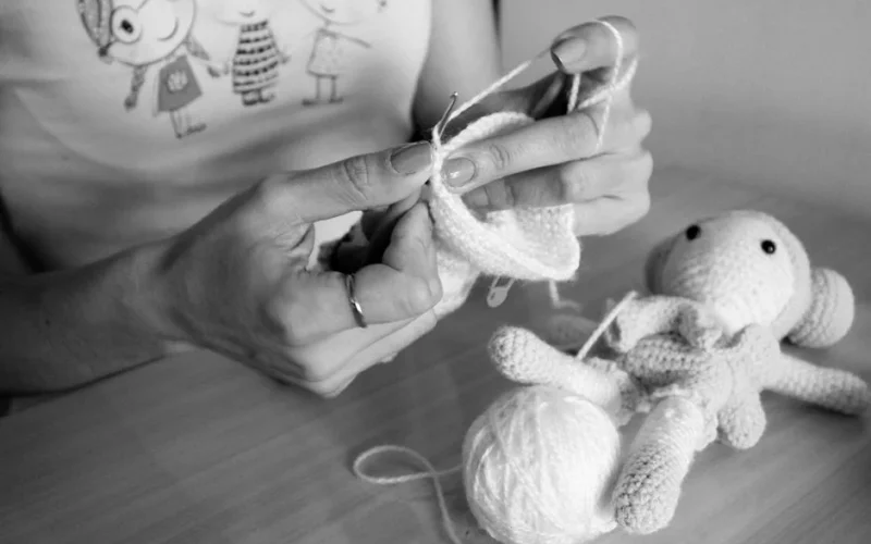 A person handcrafting a soft knitted toy using white wool indoors.