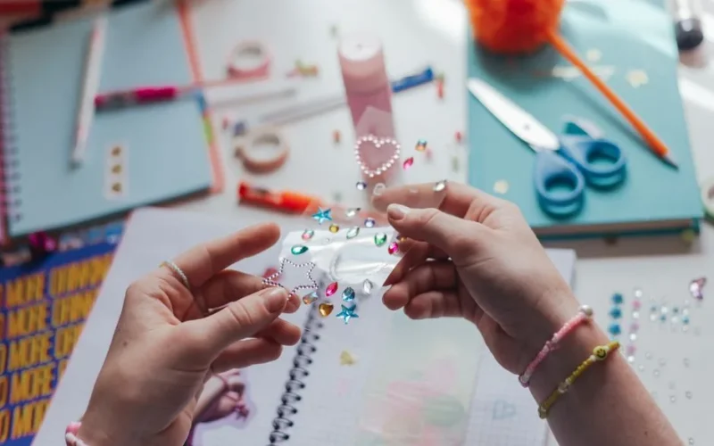 Hands decorating a notebook with colorful stickers in a creative workspace.