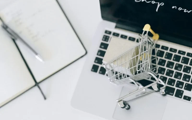 Creative depiction of online shopping with a miniature cart on a laptop keyboard.
