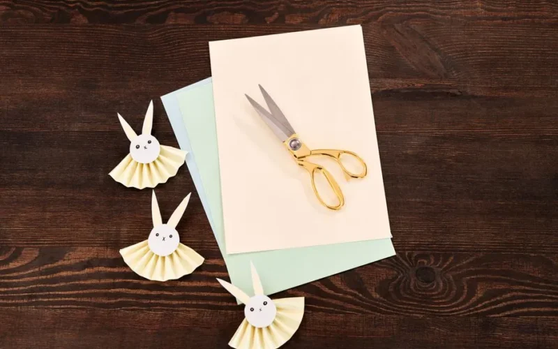 Top view of paper bunny crafts and scissors on wooden surface, perfect for Easter DIY projects.