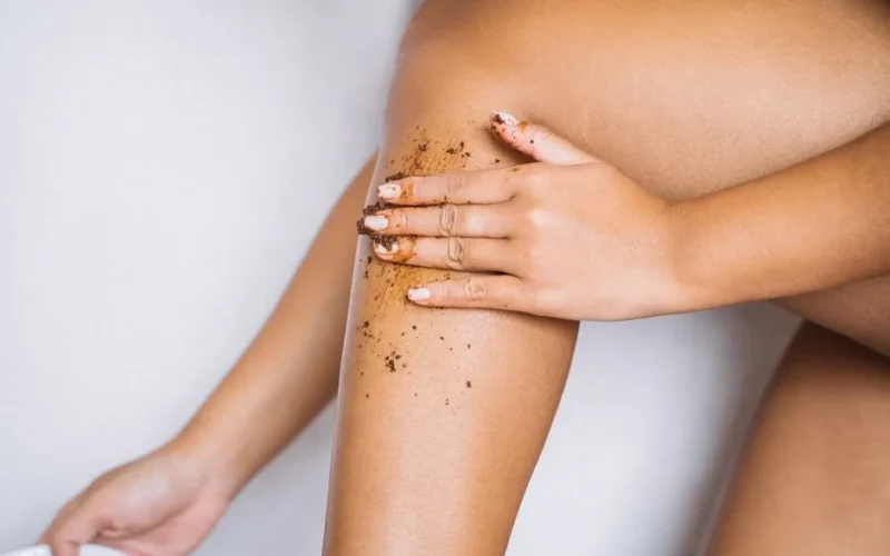Woman applying exfoliating scrub to her leg for smooth skin care.