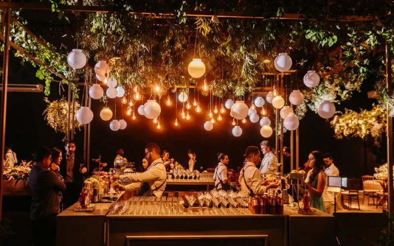 A stylish wedding reception showcasing a beautifully decorated bar with ambient lighting and lush greenery.