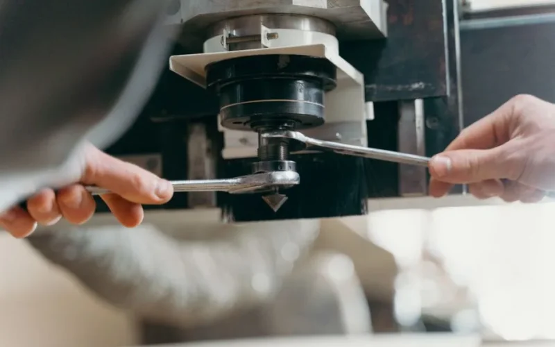 Close-up of hands adjusting a CNC machine using wrenches in an industrial setting.